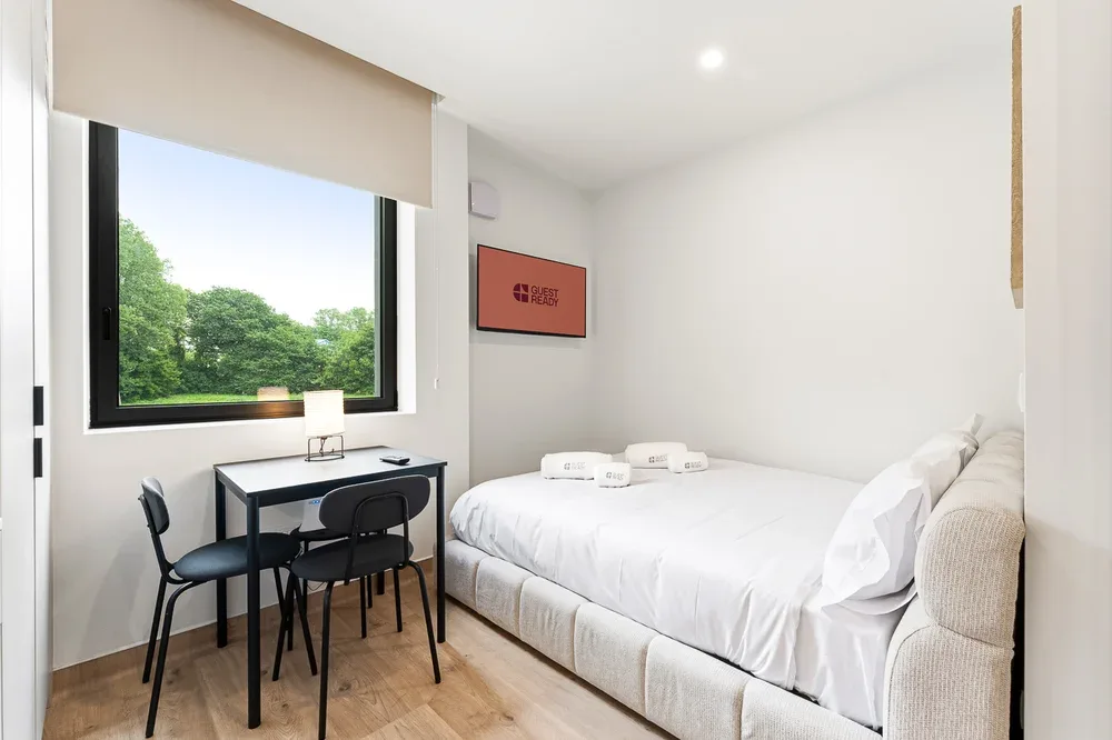 A bright bedroom with a bed beside a desk and a large window.