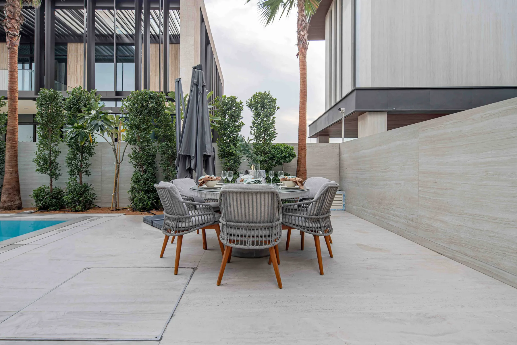 Una zona de comedor al aire libre con mesa y asientos junto a una piscina.