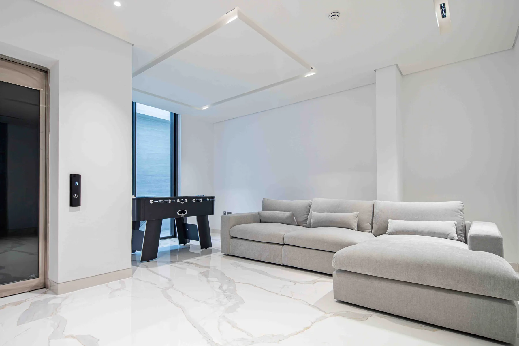 Una sala luminosa con un sofá en forma de L y una mesa de futbolín.