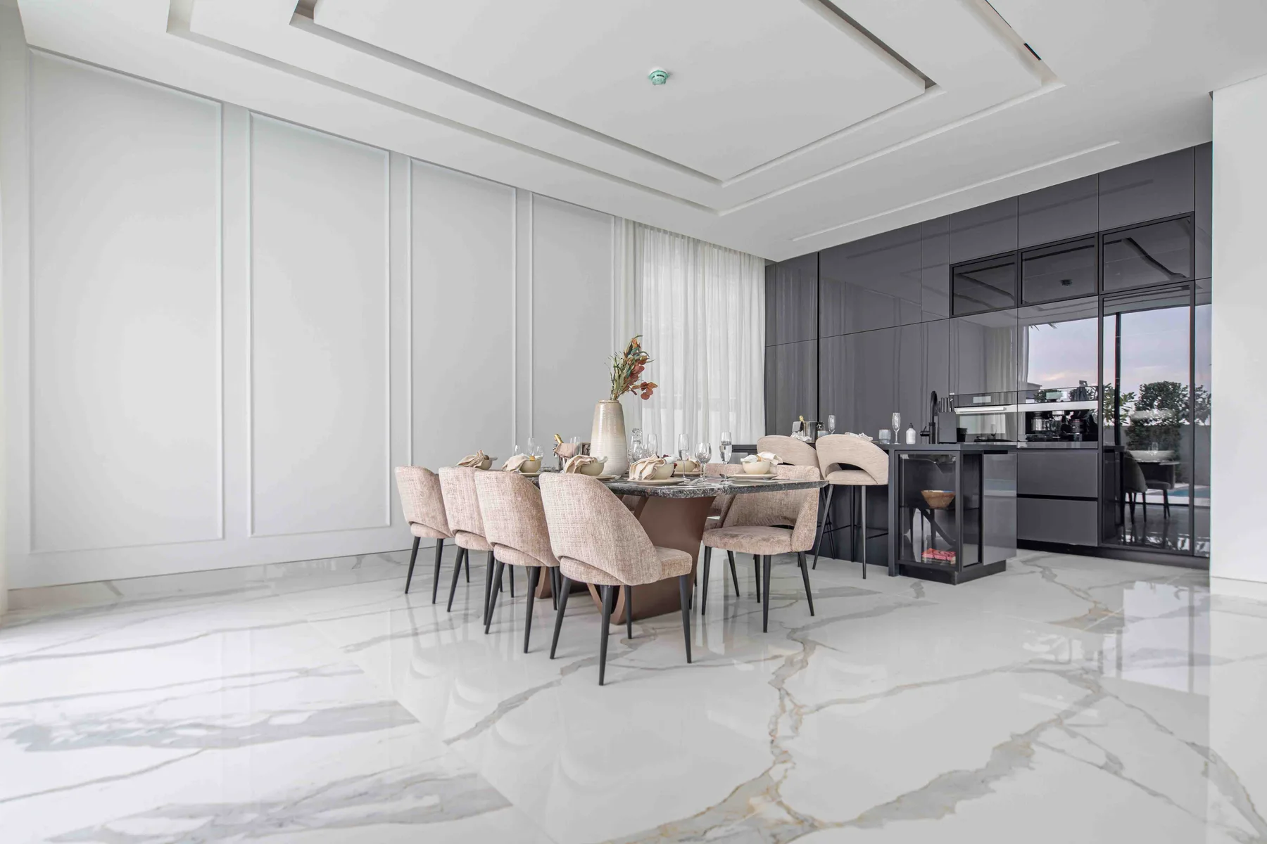 Un comedor luminoso con asientos tapizados alrededor de una mesa junto a una cocina oscura.