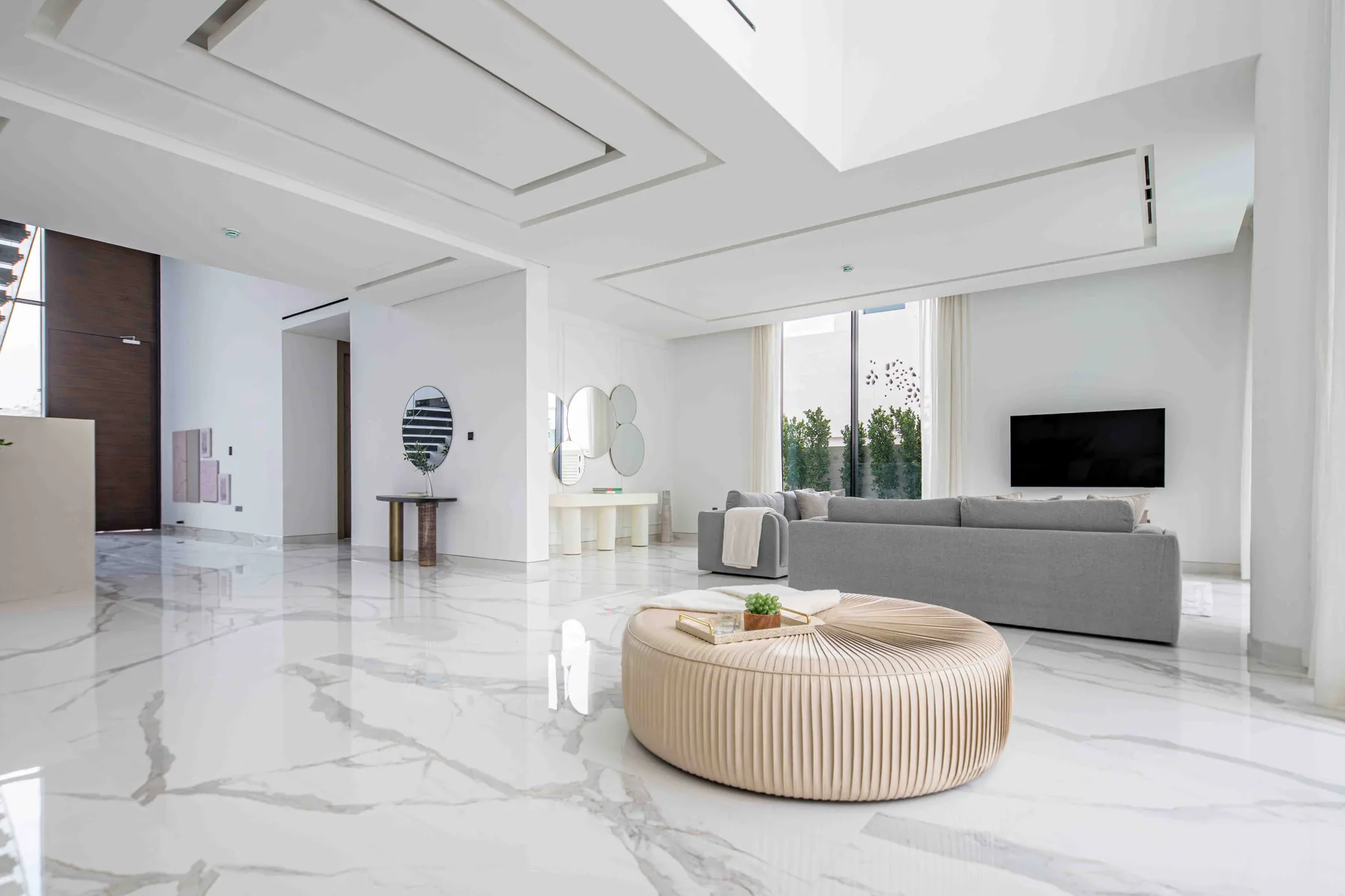 Una sala de estar moderna y luminosa con un sofá gris y una mesa de centro redonda tapizada.
