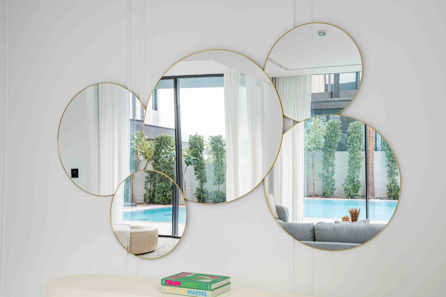 Una luminosa sala tiene grandes ventanales con vistas a una piscina y vegetación.