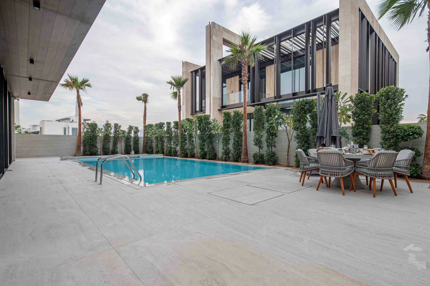 Una piscina al aire libre junto a un edificio moderno, con asientos de patio y vegetación.