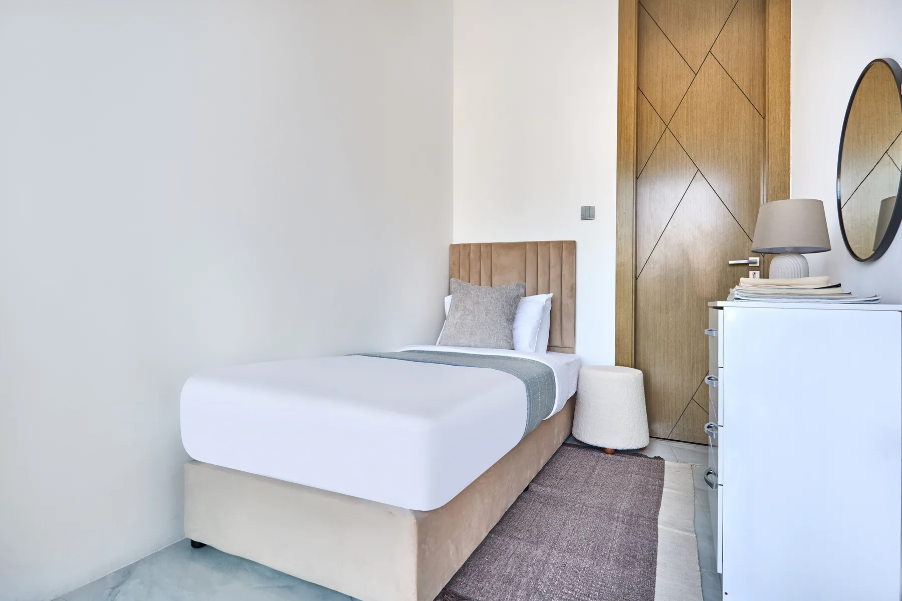 Un dormitorio con una cama, ropa de cama clara y una mesita de noche.