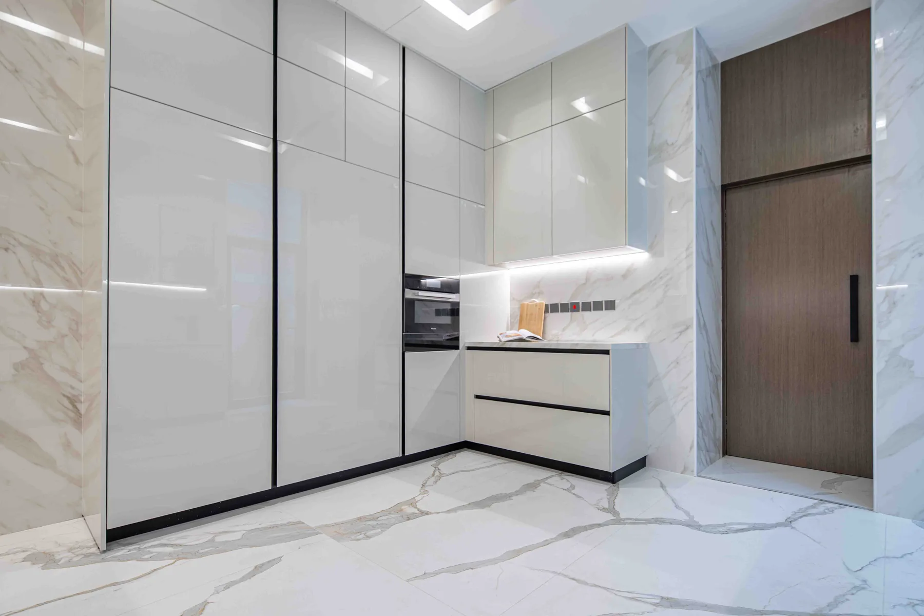 Una cocina moderna con armarios brillantes, un horno empotrado y un suelo de piedra clara.