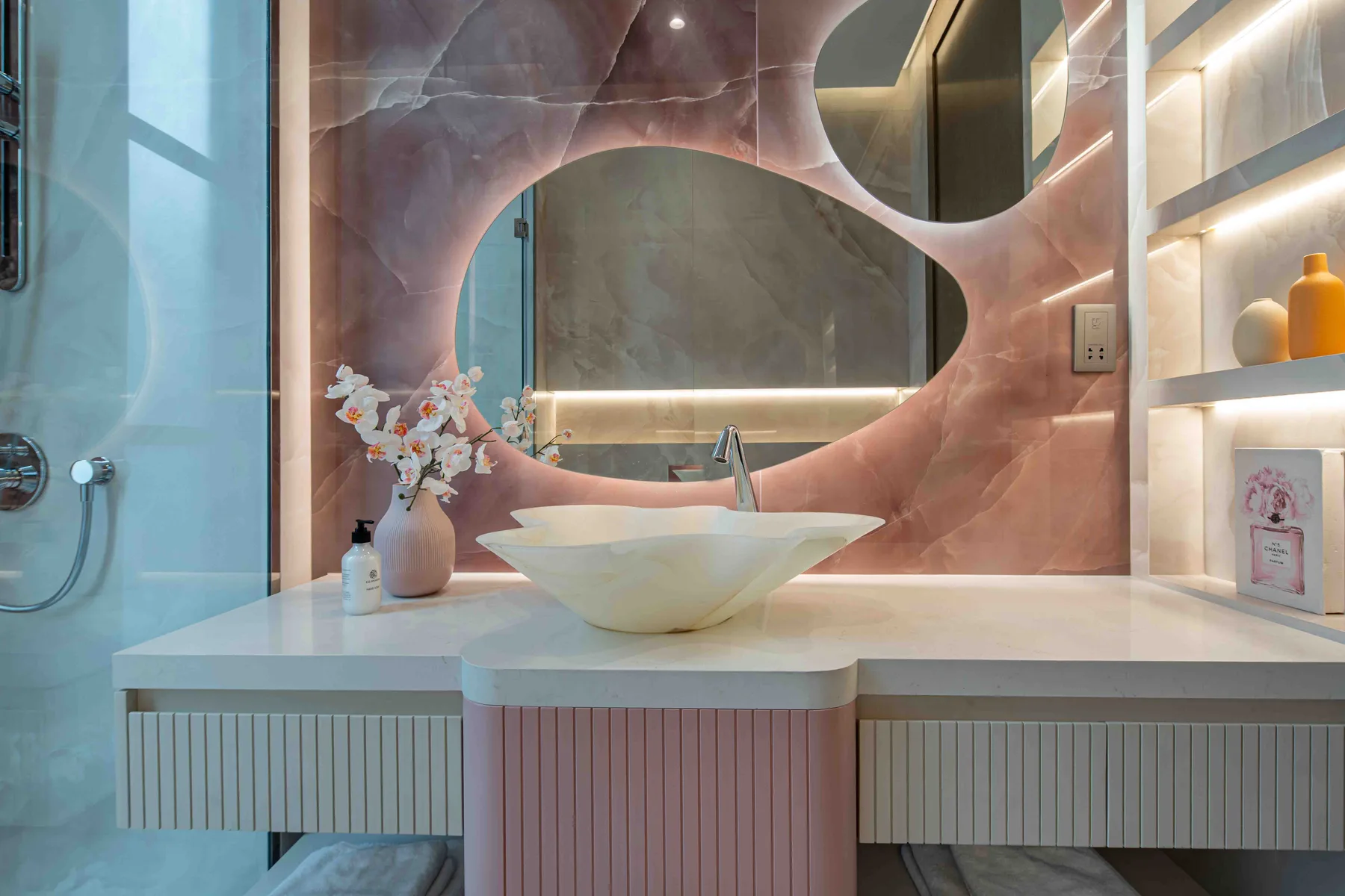 Un tocador de baño con lavabo sobre encimera, un espejo grande y estantes iluminados.