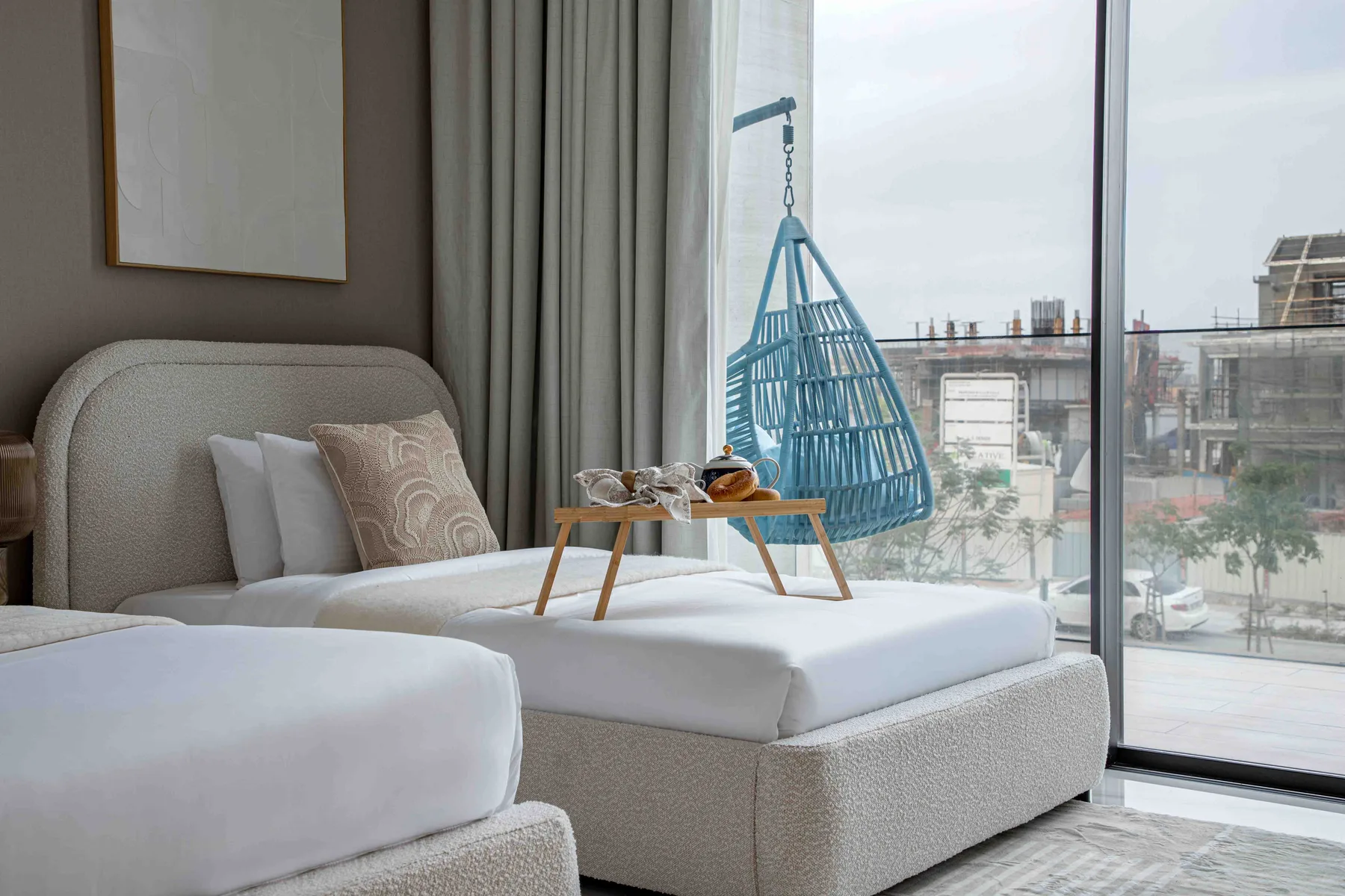 Dormitorio con dos camas y una silla colgante azul junto a una gran ventana.