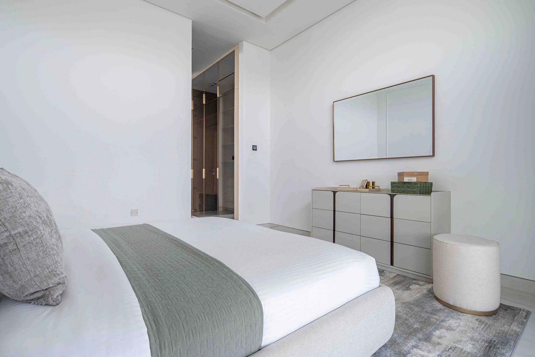 Un dormitorio luminoso tiene una cama bien tendida y una cómoda bajo un espejo.