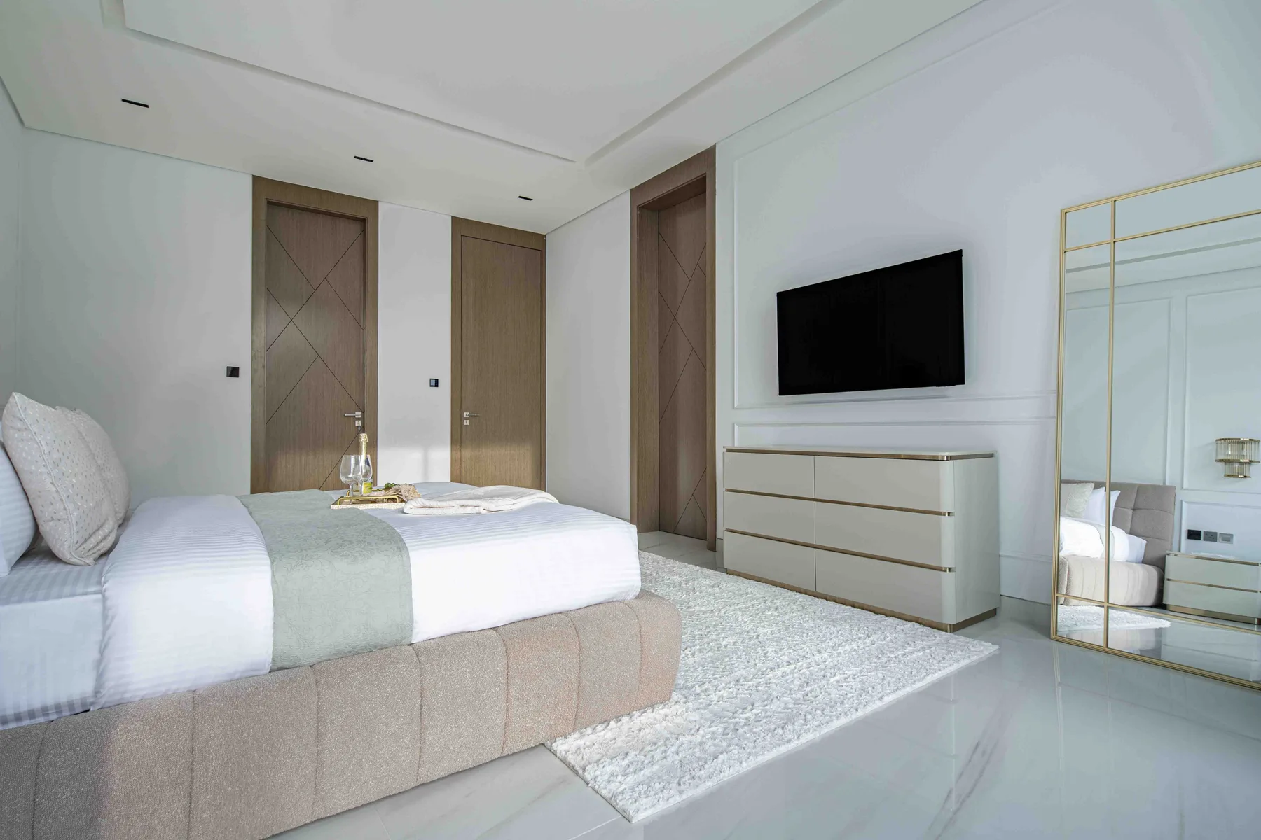 Un dormitorio luminoso con una cama tendida y un televisor montado en la pared.