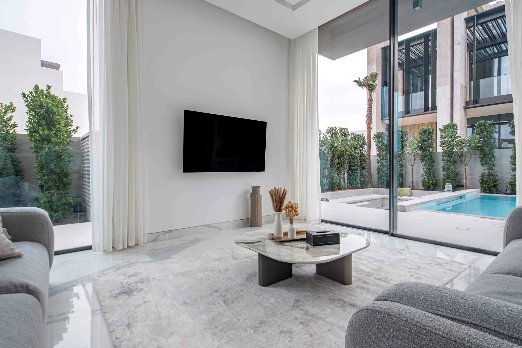 Una sala luminosa con un televisor en la pared y vistas a la piscina.