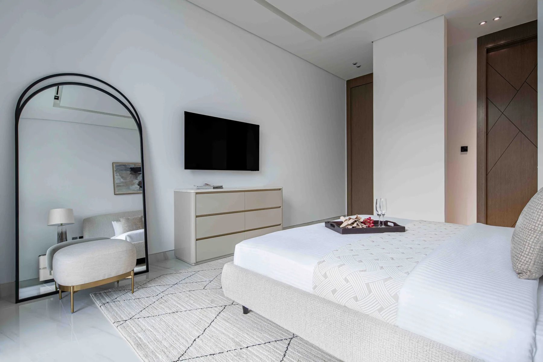 Un dormitorio luminoso con una cama grande, un televisor y un espejo de cuerpo entero arqueado.
