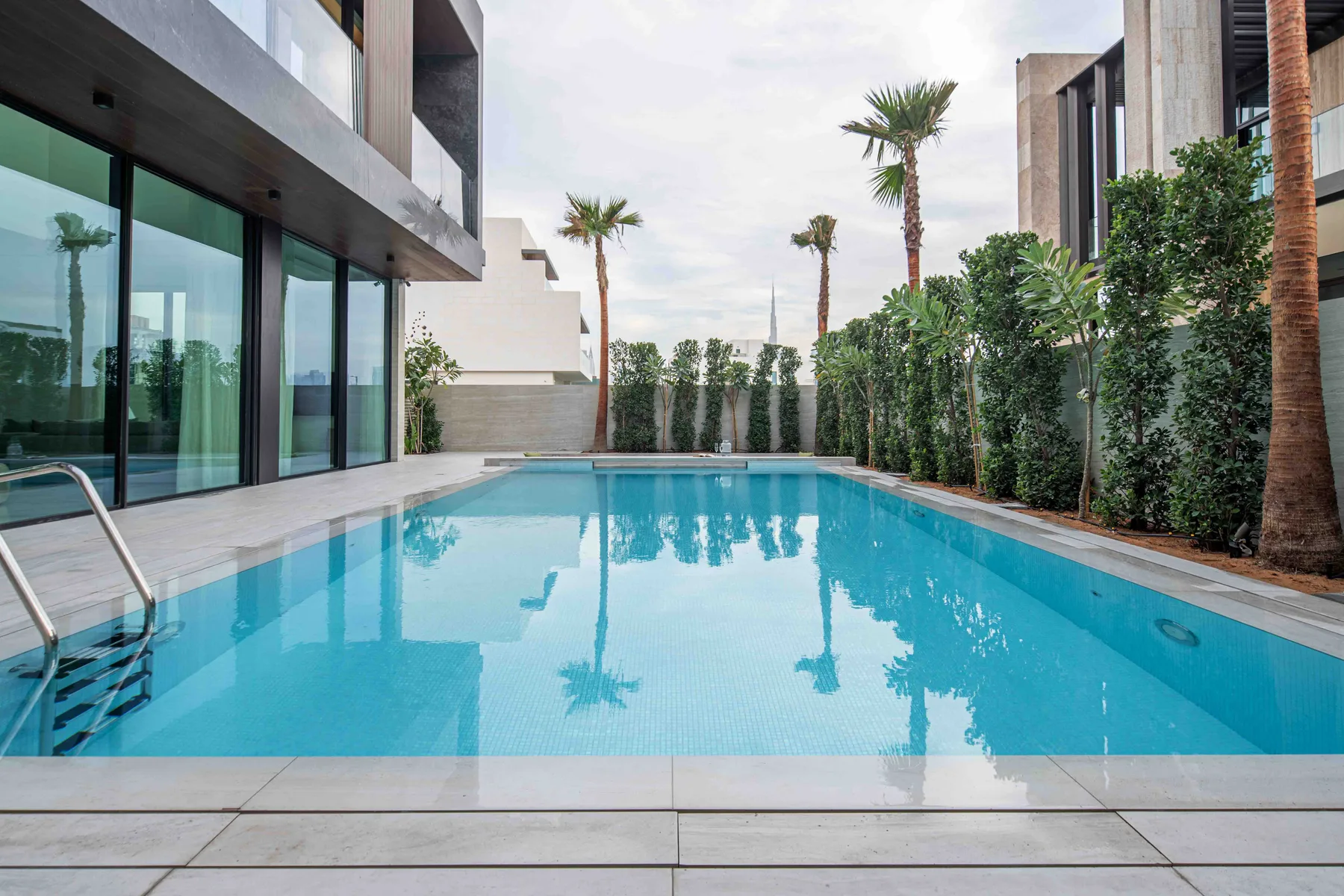 Una piscina al aire libre junto a un edificio moderno, con palmeras y vegetación.