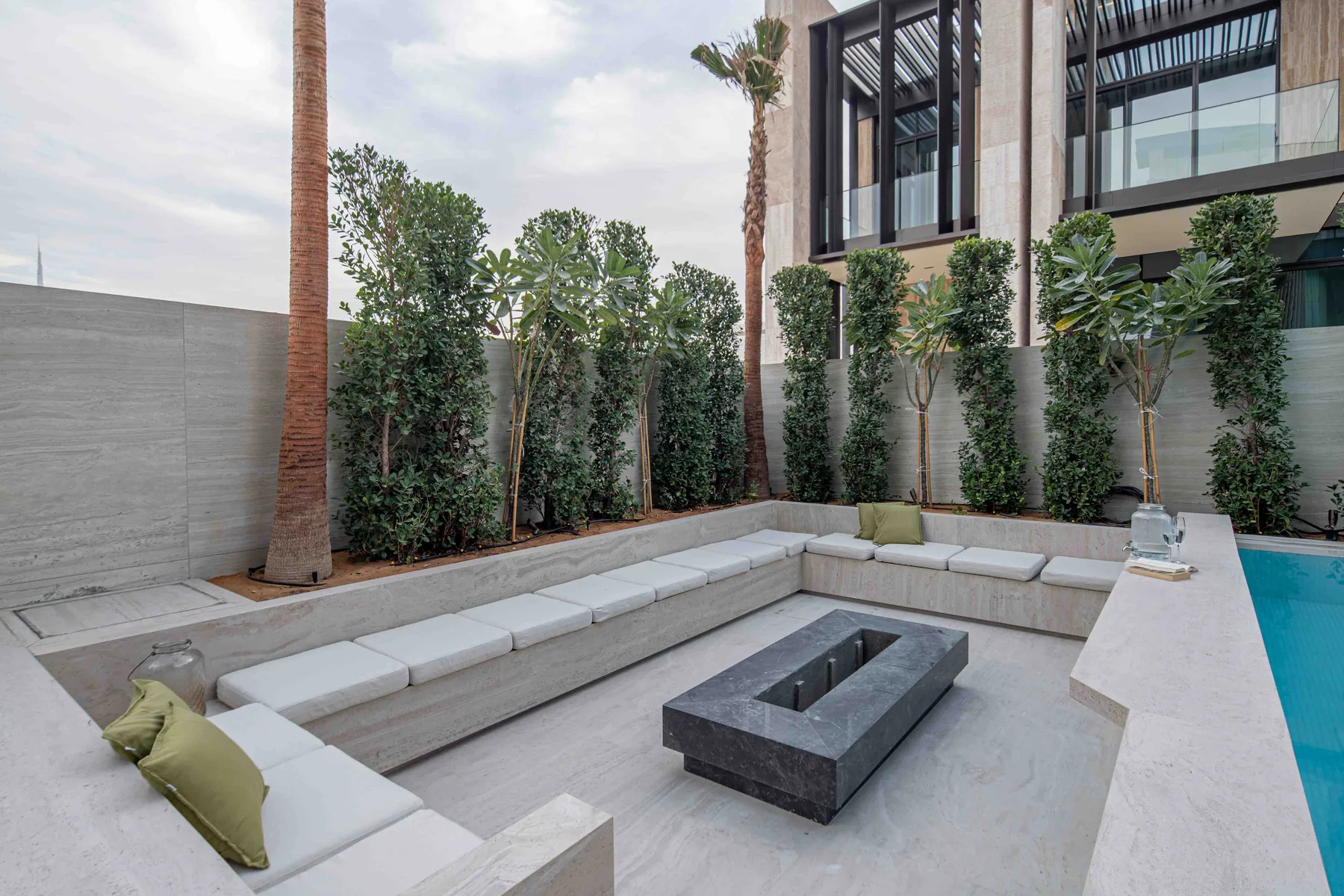 Una zona de estar al aire libre con asientos empotrados alrededor de una mesa baja, junto a una piscina.