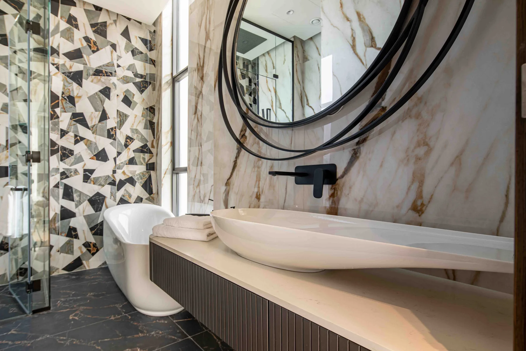 Un baño moderno con lavabo sobre encimera, espejo redondo y ducha de vidrio.