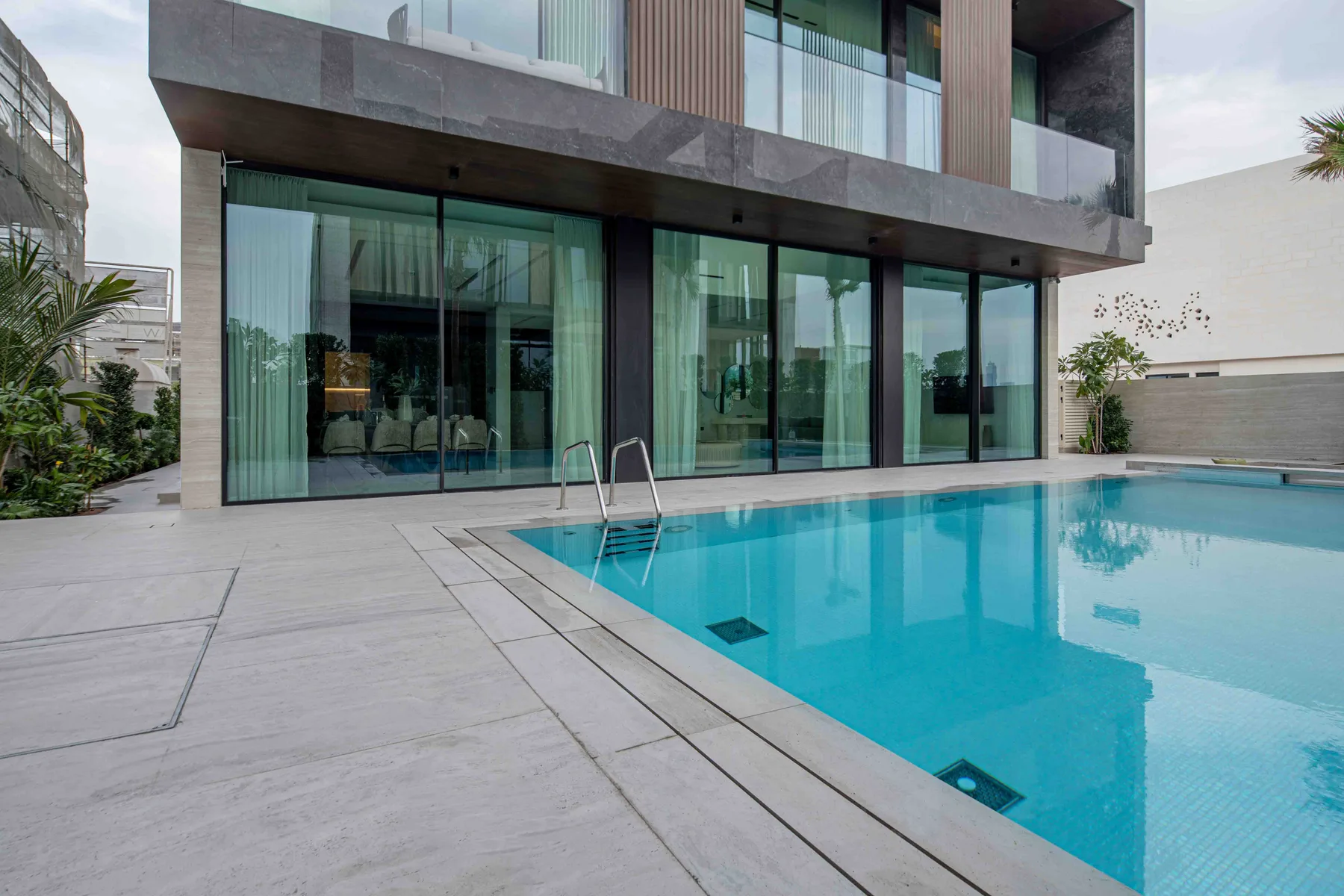 Una piscina está junto a un edificio moderno con amplias puertas de vidrio.