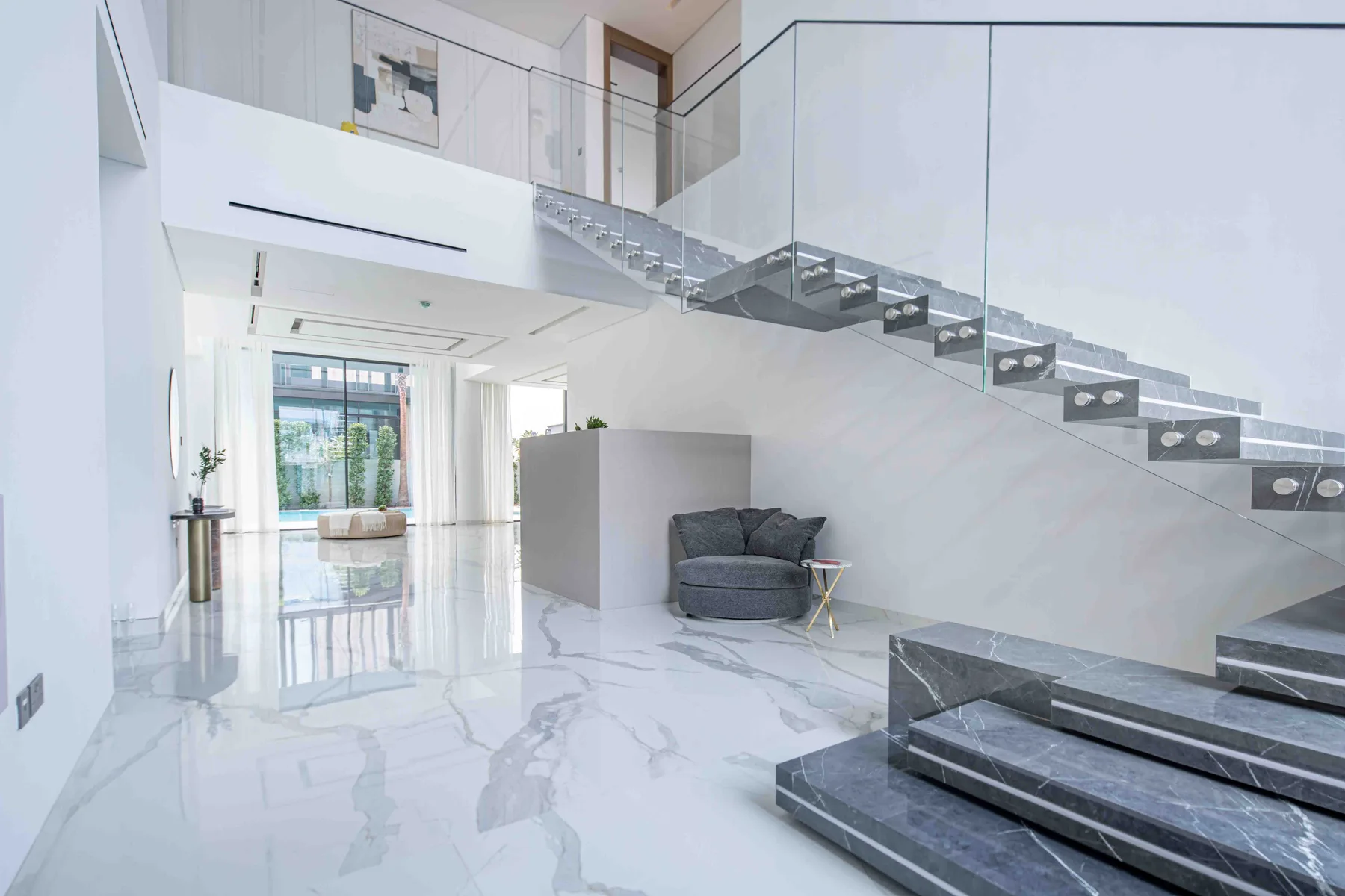 Una luminosa sala de estar moderna con una escalera y barandilla de vidrio.