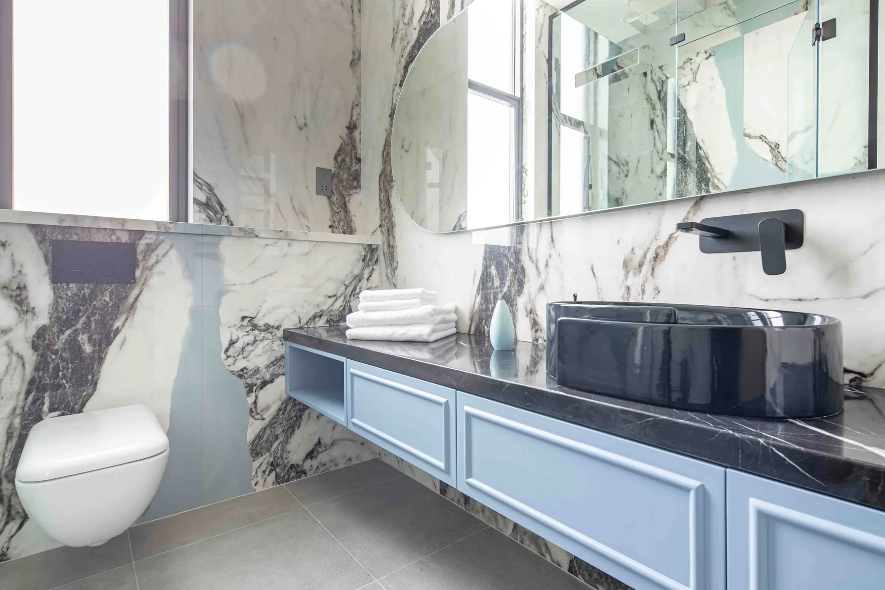 Un baño luminoso con un inodoro suspendido y un largo mueble de lavabo bajo un espejo.