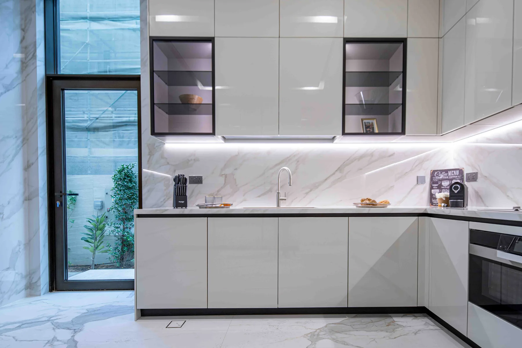 Una cocina moderna con gabinetes claros, un salpicadero con vetas y una ventana alta.