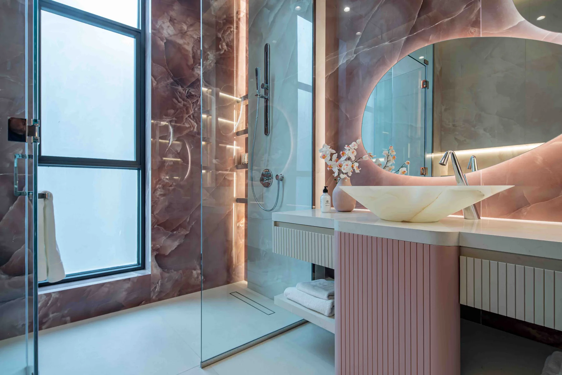 Un baño moderno con ducha de vidrio, lavabo escultural y una ventana grande.