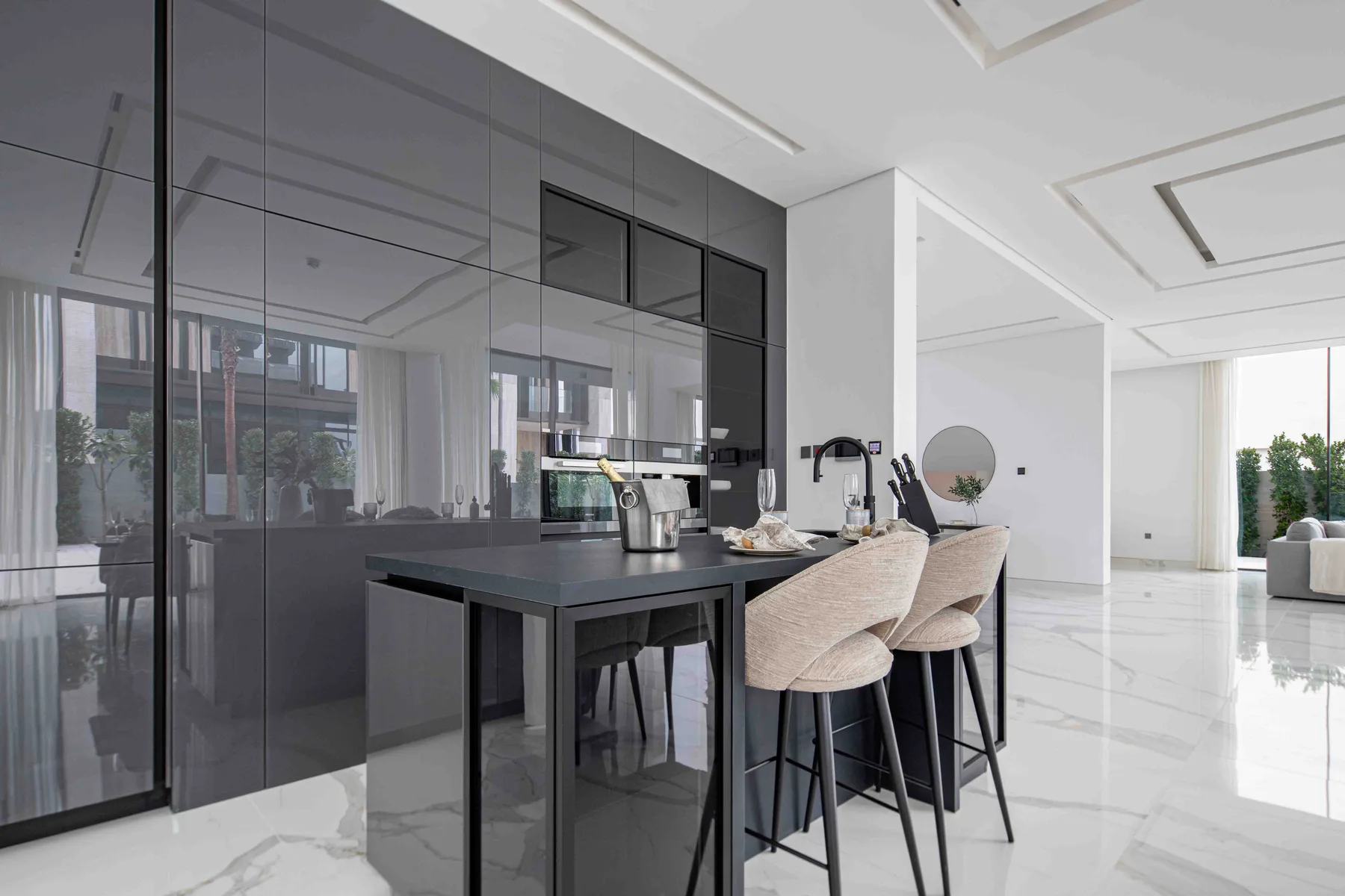 Una cocina moderna con una isla oscura, asientos claros y pisos brillantes.