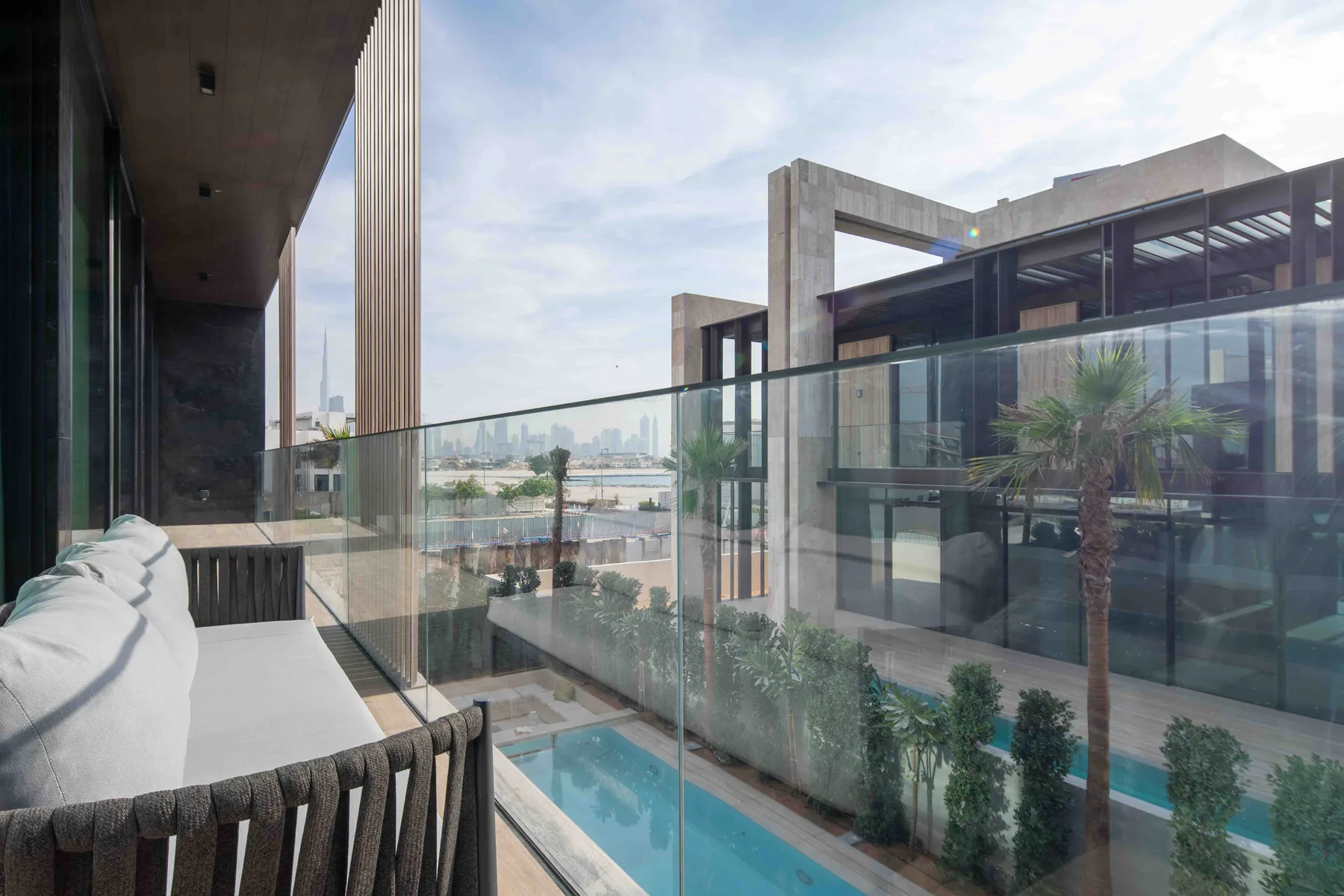 Una zona de estar en un balcón da a una piscina y edificios modernos.