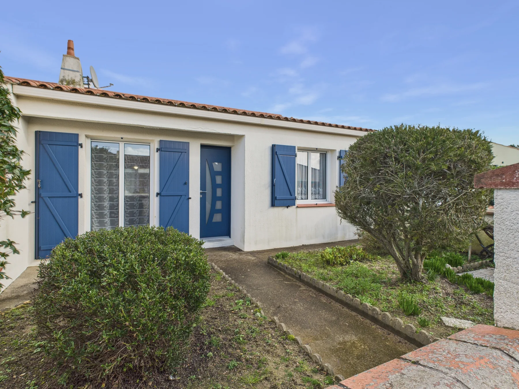 A white house exterior with blue shutters and a path leading to the entrance.