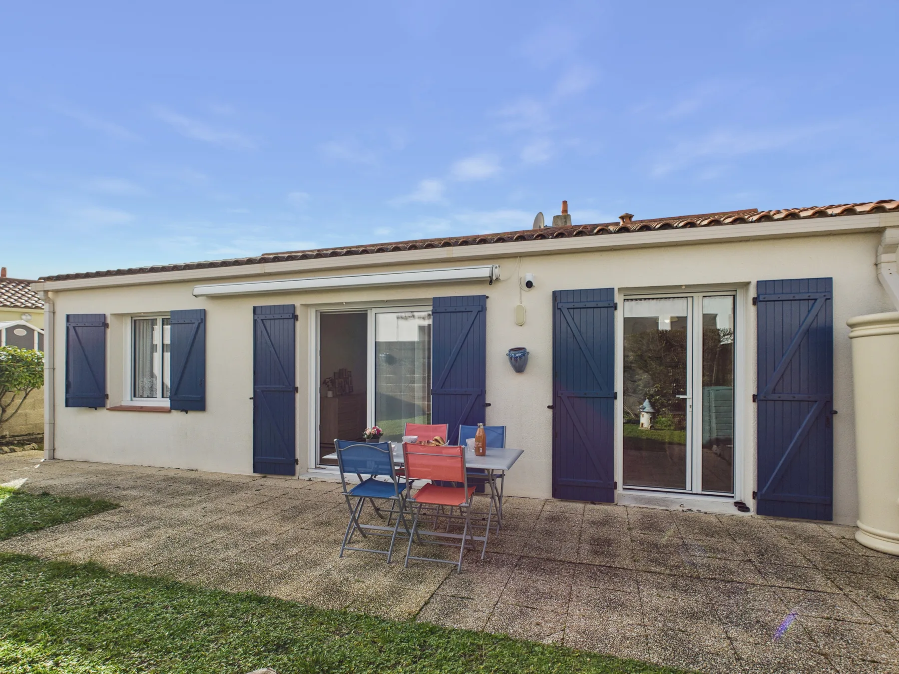 A house exterior with blue shutters and a paved patio with outdoor seating.