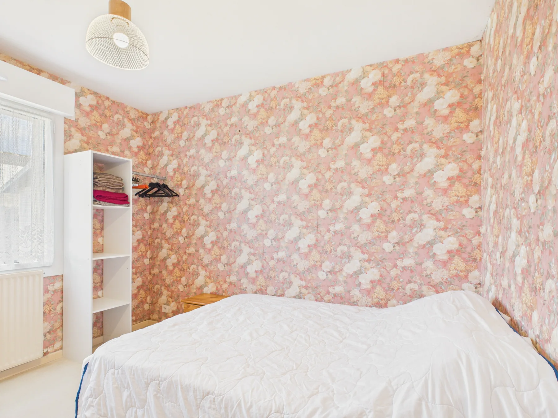 A bedroom with a bed covered in white bedding and floral wallpaper.