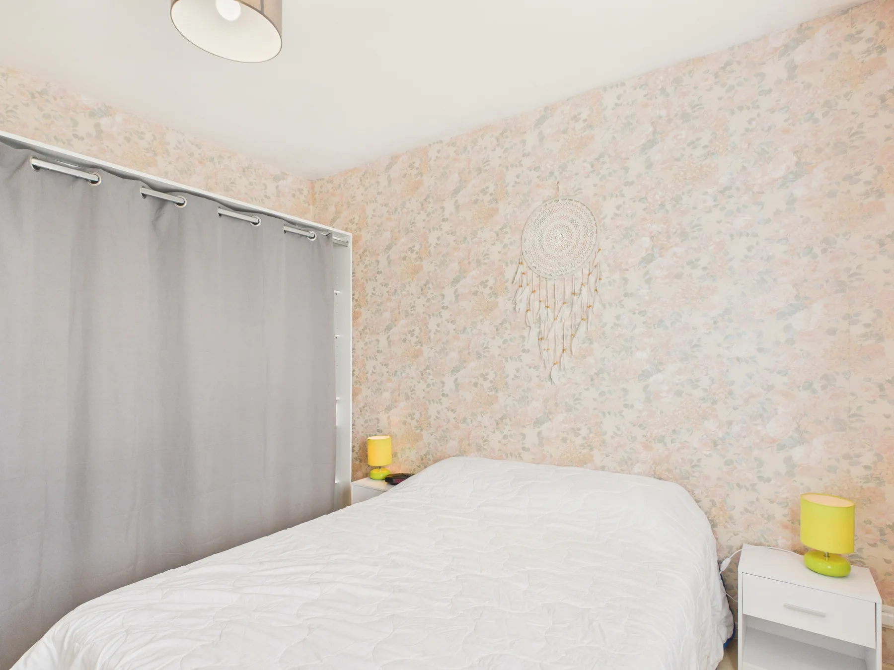 A bedroom with a bed, gray curtains, and pale patterned walls.