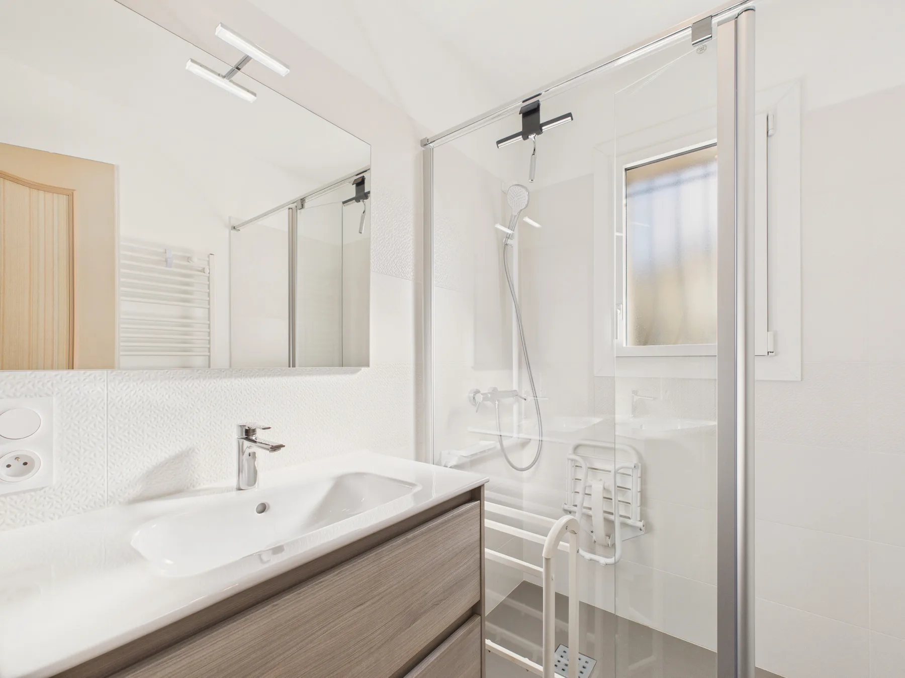 A bright bathroom with a sink, mirror, and glass shower.
