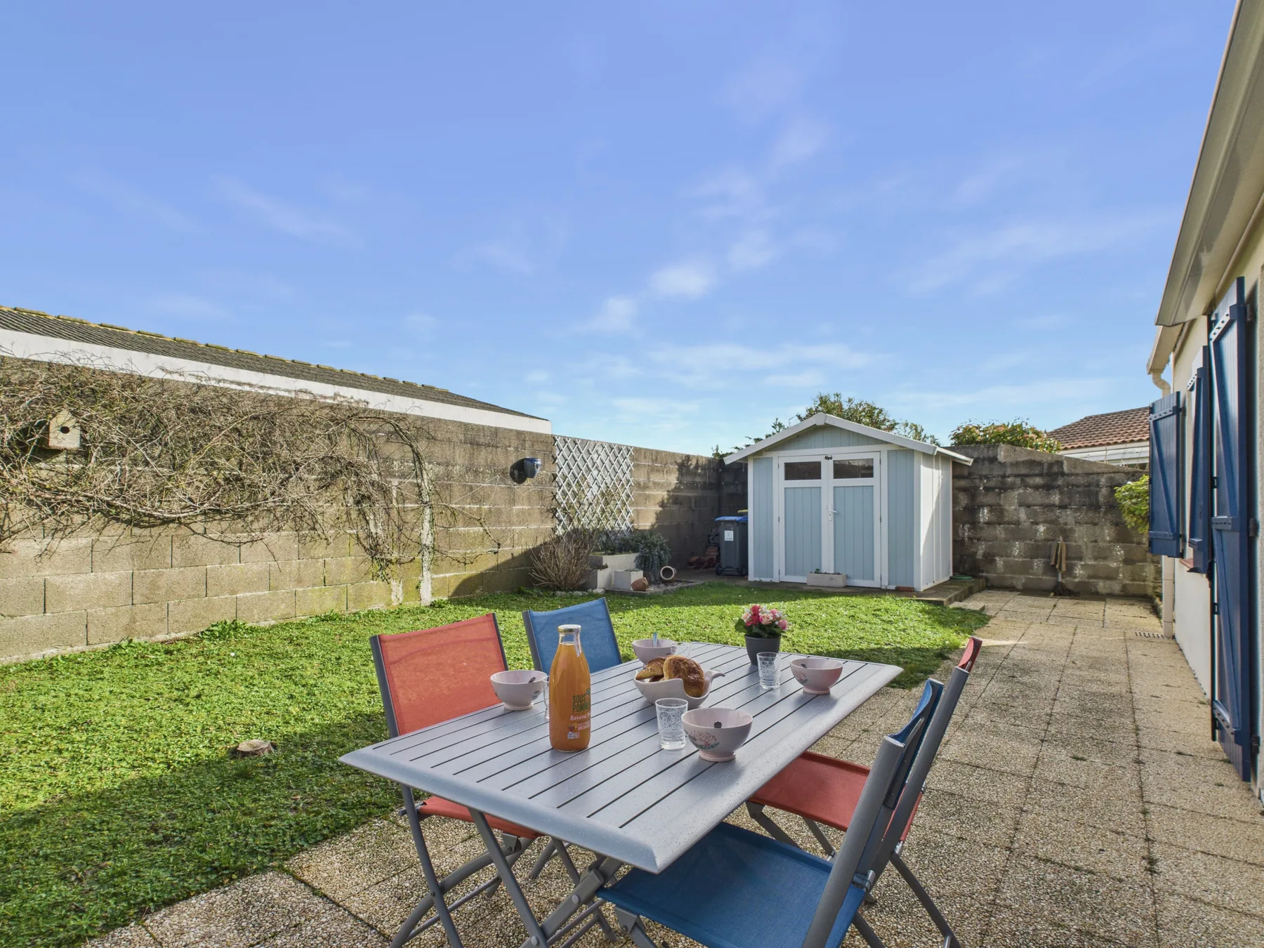 A paved backyard patio with outdoor seating, a table, and a small shed.