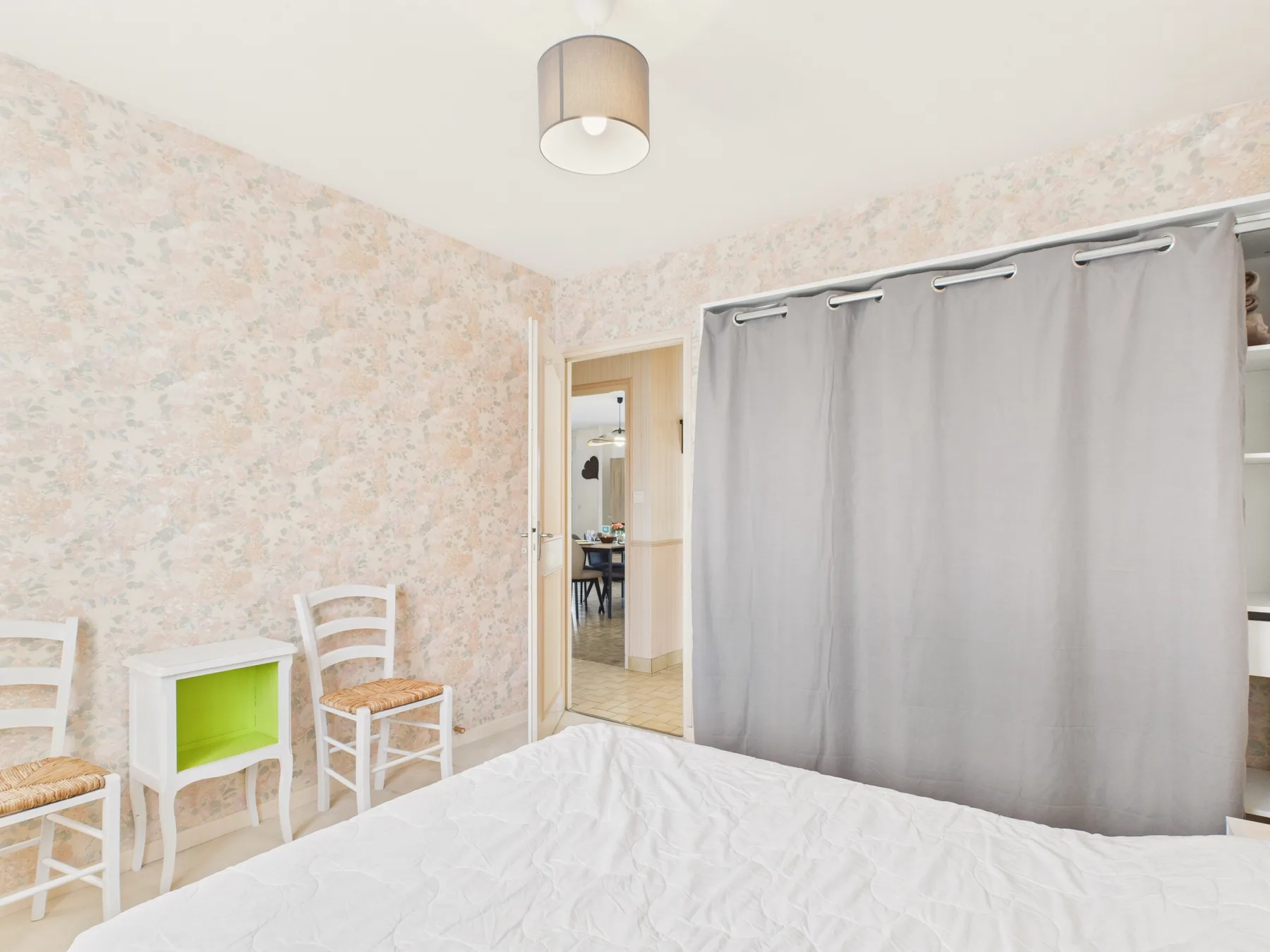 A bedroom with a bed, white chairs, and a gray curtain.