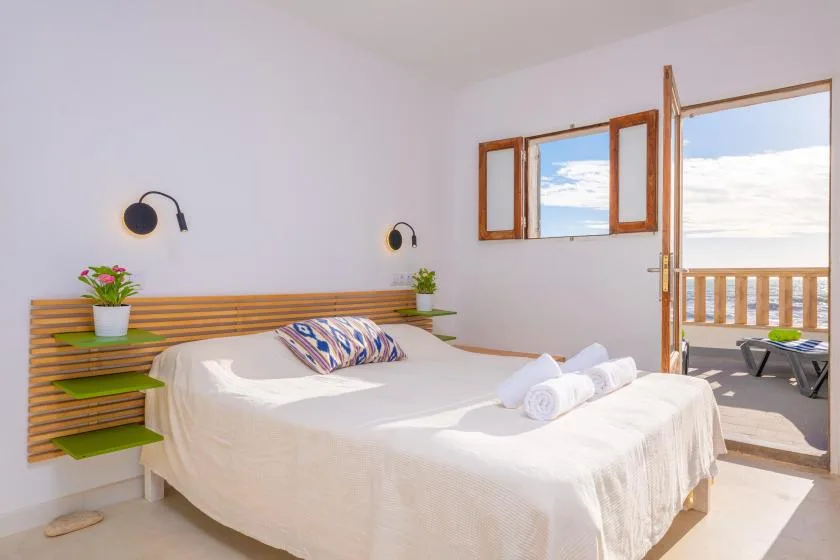Un dormitorio luminoso con una cama doble junto a una puerta abierta al balcón.