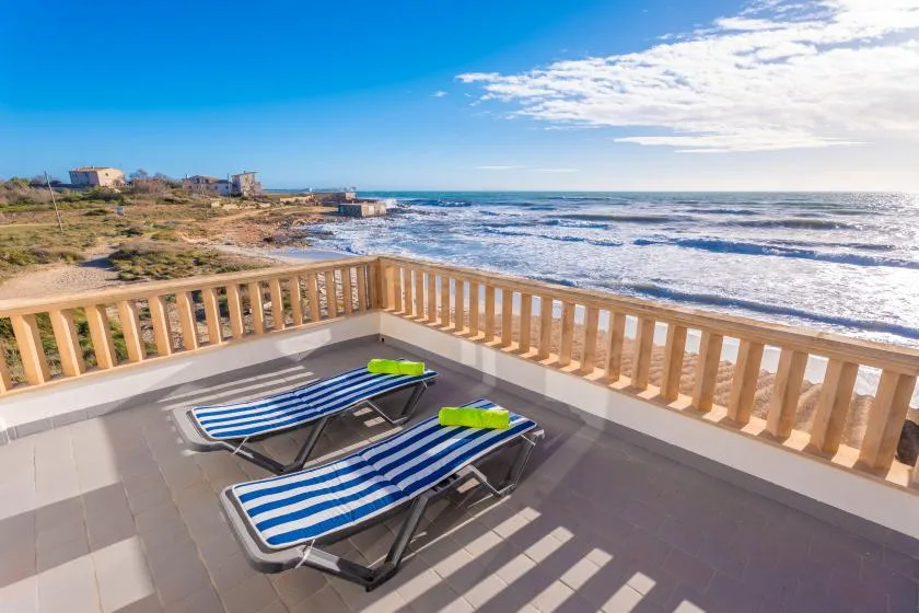 Una terraza junto al mar con suelo de baldosas mira al océano y tiene tumbonas a rayas junto a la barandilla.