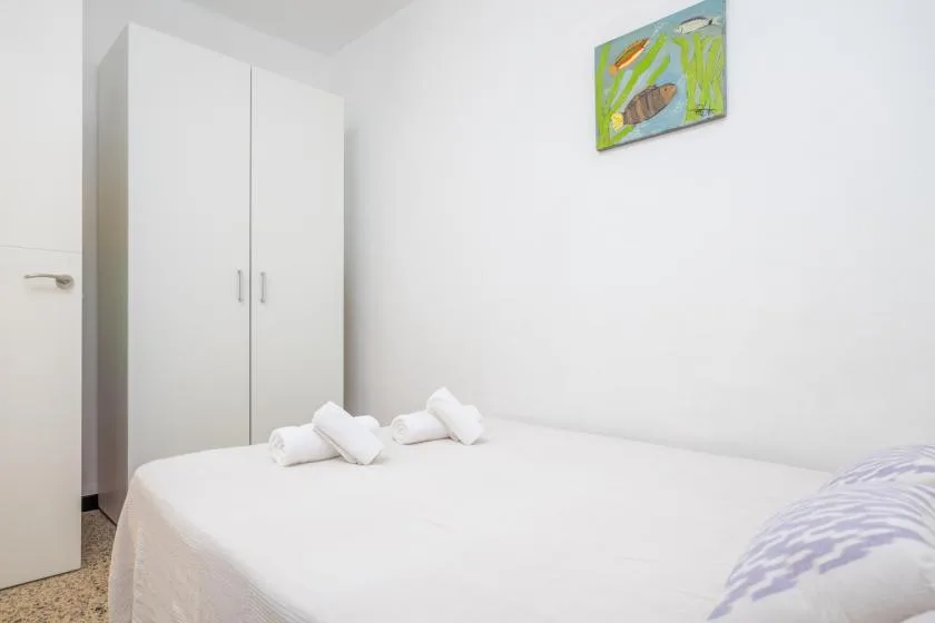 Un dormitorio con una cama blanca, toallas dobladas y un armario alto.