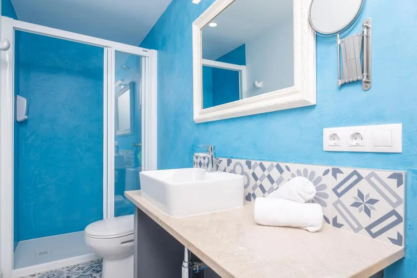 Un baño azul luminoso con lavabo, espejo y ducha.