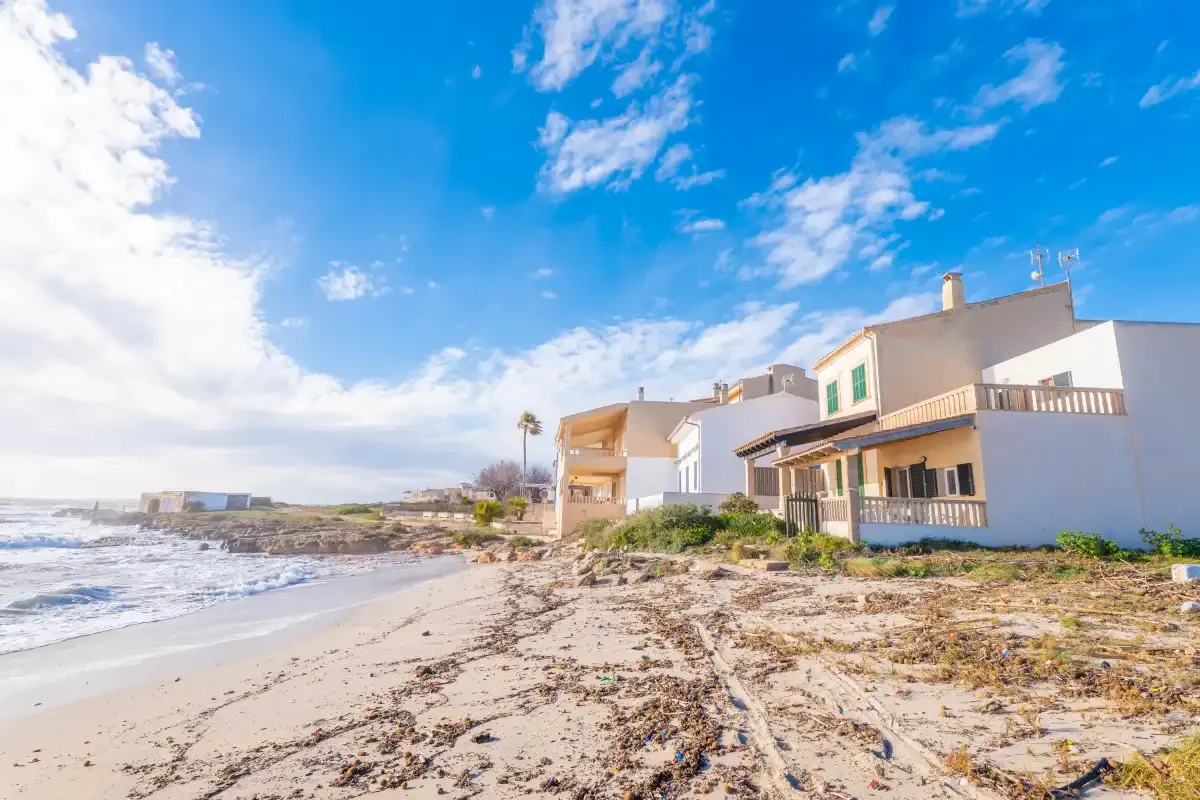 Casas costeras junto a una playa de arena bajo un cielo azul despejado.
