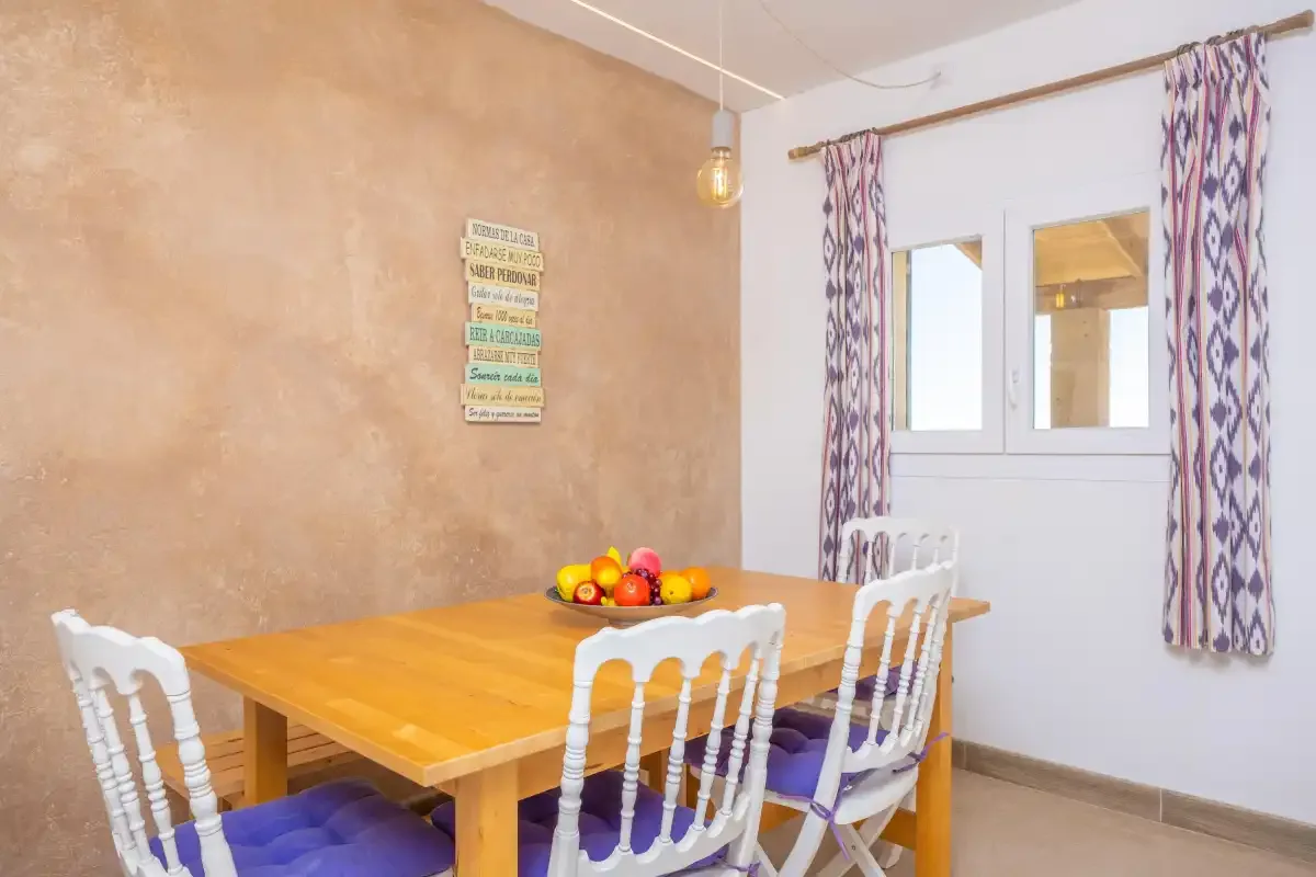 Un comedor con una mesa de madera, sillas blancas y una ventana con cortinas.