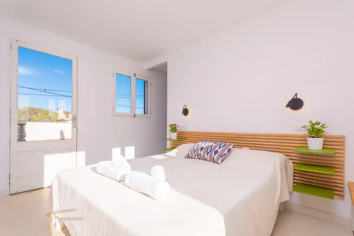 Un dormitorio luminoso con una cama, cojines a rayas y listones de madera en la pared.