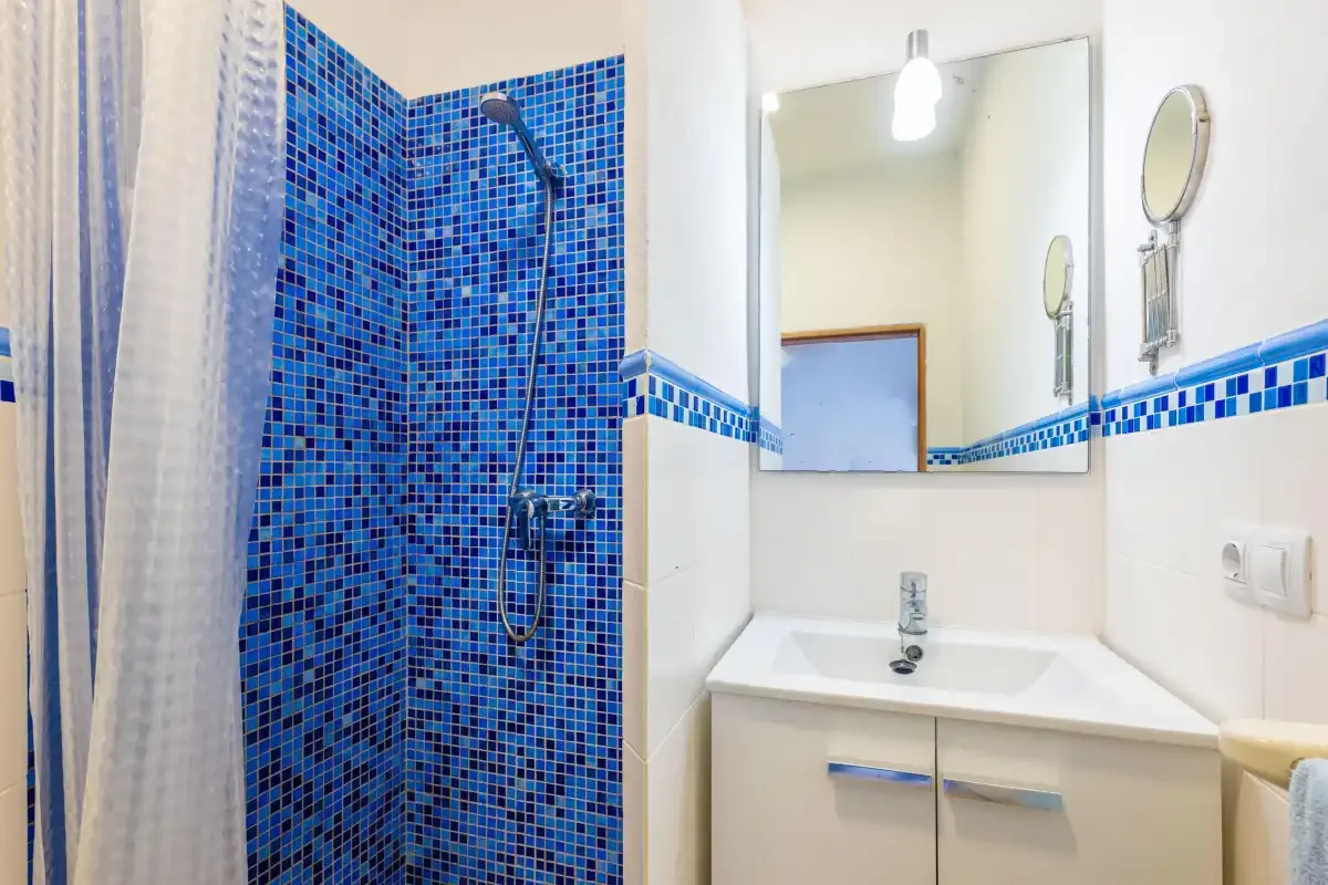Un baño con una zona de ducha de azulejos azules y un lavabo bajo un espejo.