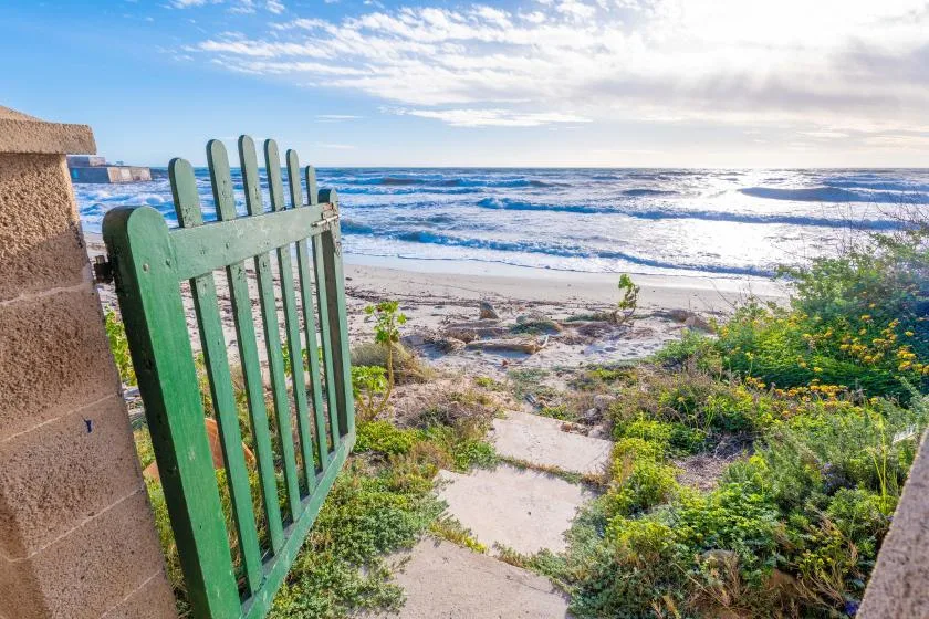 Un sendero arenoso pasa por una puerta verde hacia el océano.
