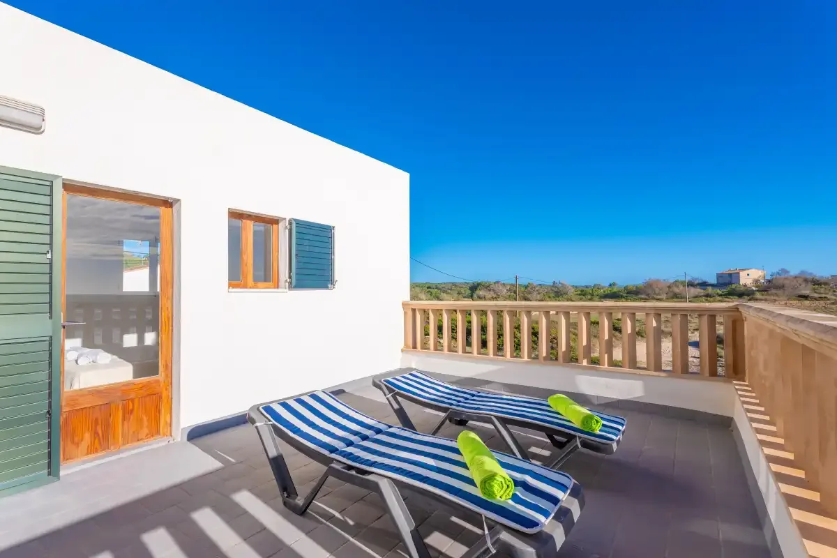 Una terraza soleada tiene tumbonas a rayas junto a una barandilla de madera.
