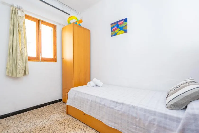 Un dormitorio luminoso con una cama individual, un armario de madera y una ventana.