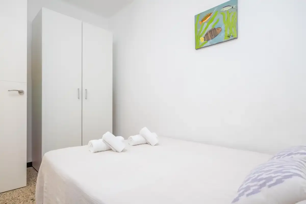 Un dormitorio luminoso con una cama blanca y un armario.