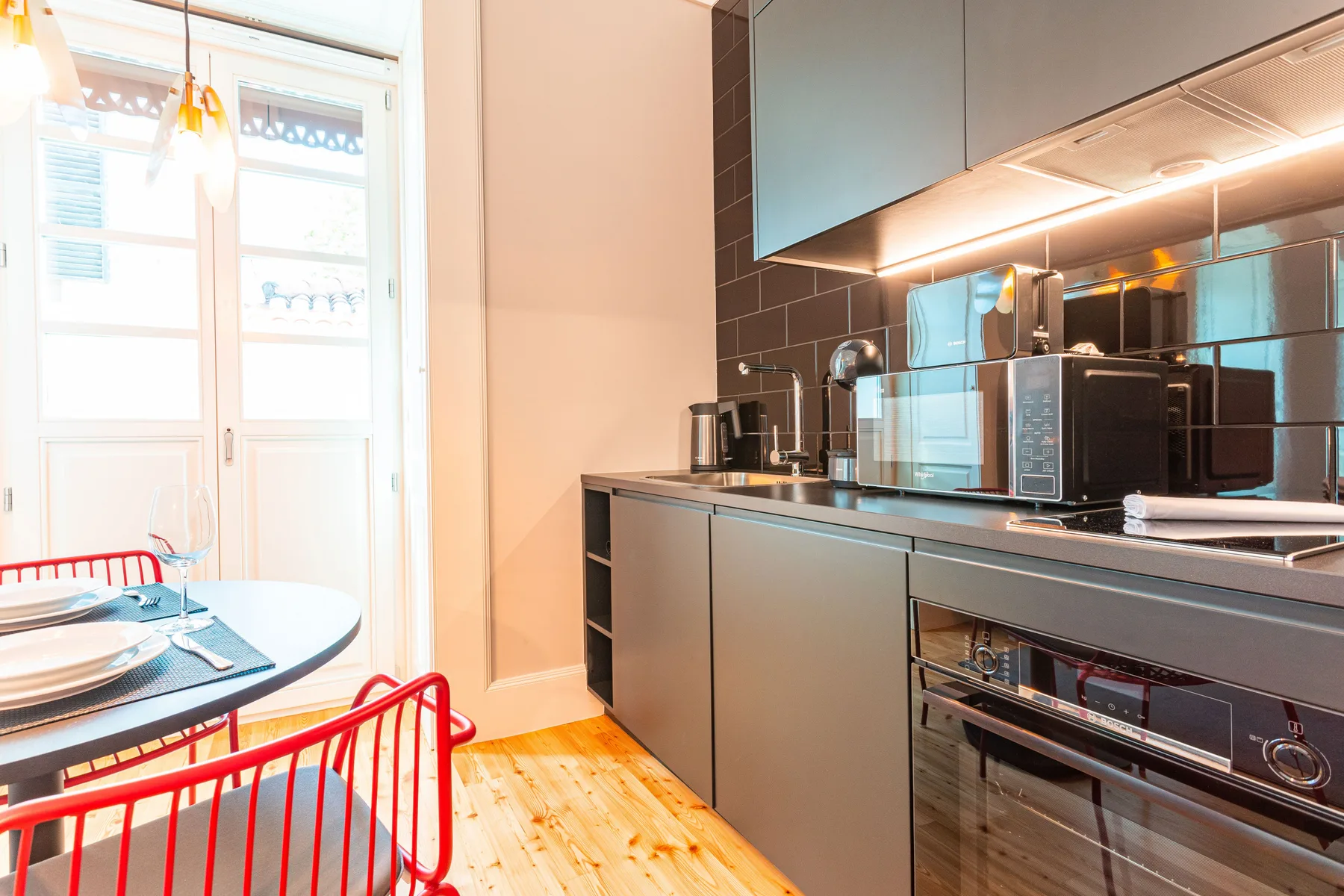 Una cocina compacta con armarios oscuros, electrodomésticos y una pequeña mesa junto a la ventana.