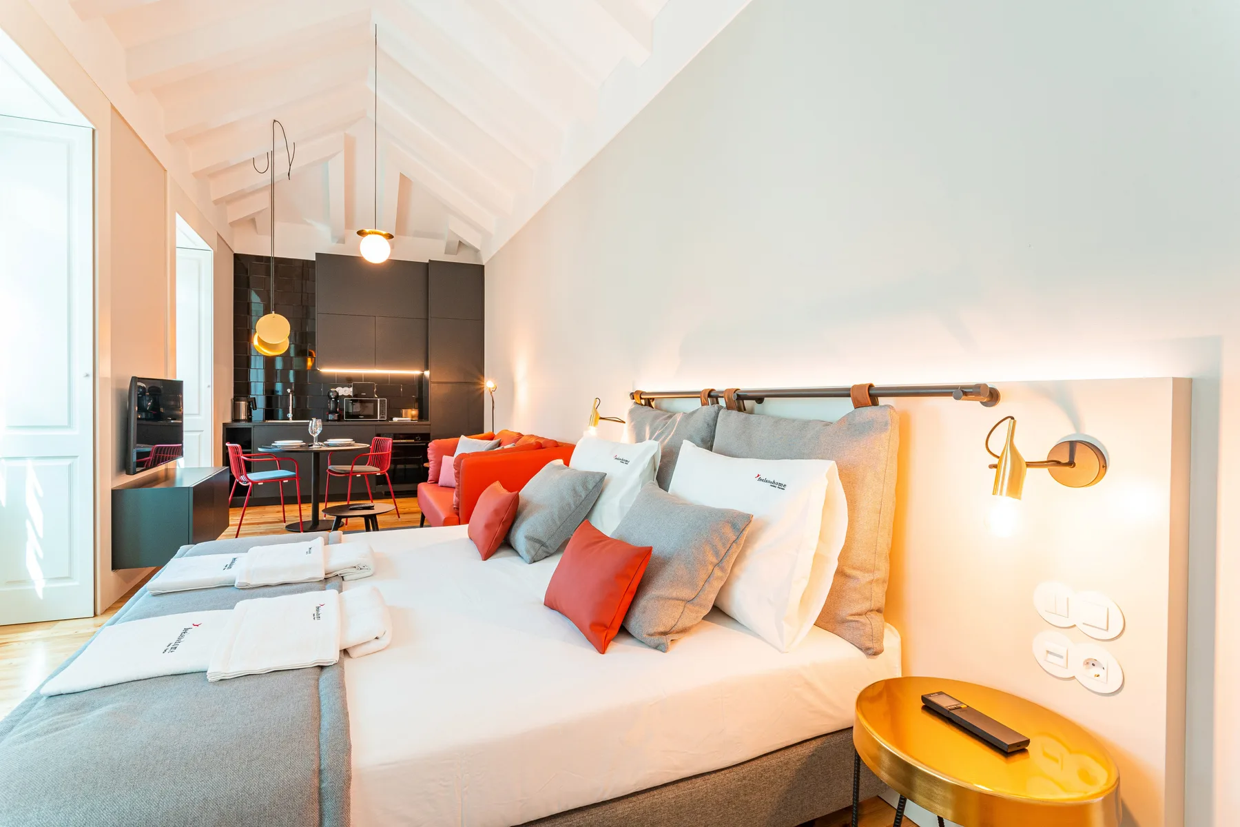 Un dormitorio luminoso con una cama y una cocina compacta al fondo.