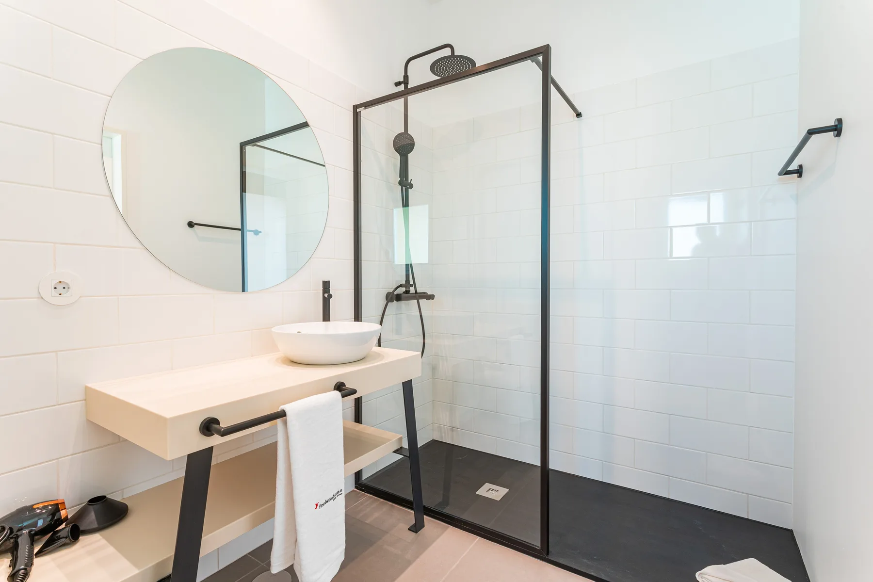 Un baño luminoso con lavabo, espejo redondo y ducha de vidrio.