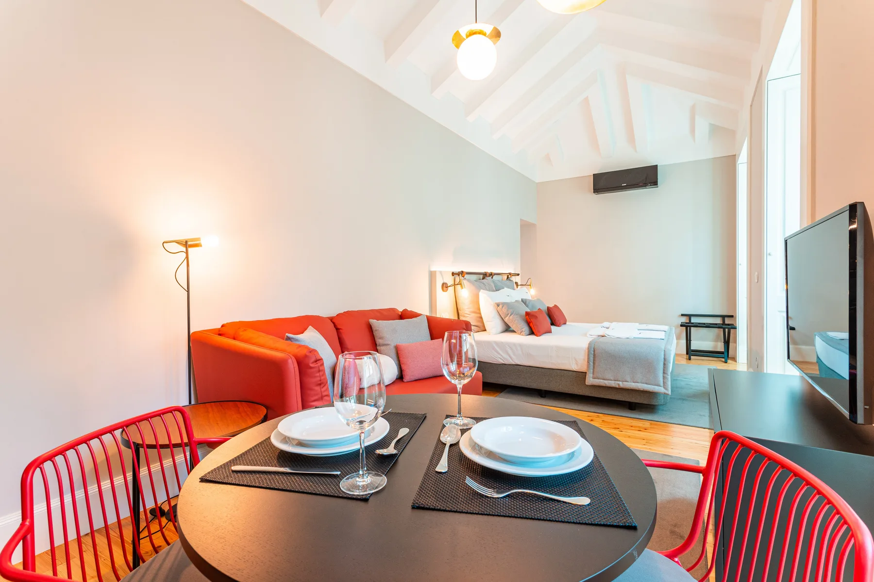 Una luminosa zona de estudio tiene una mesa redonda y una cama.