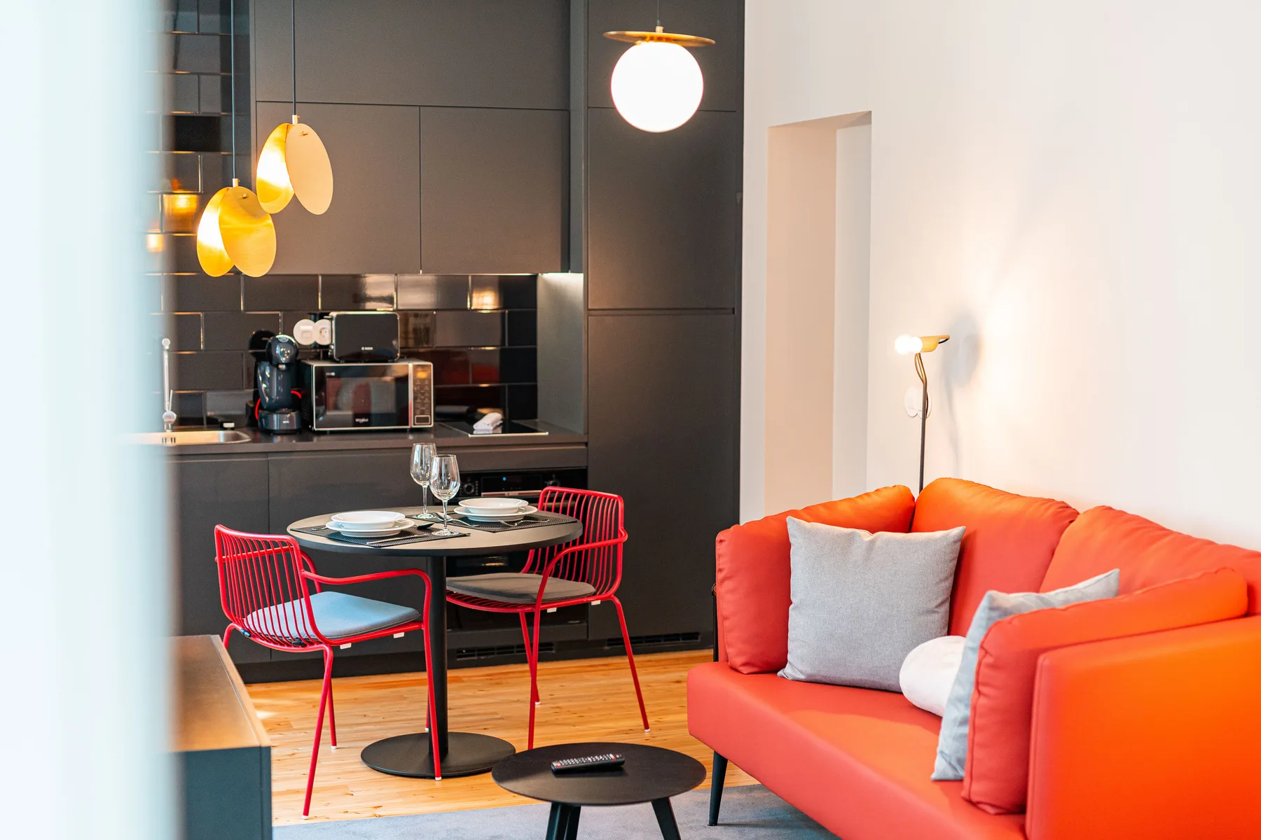 A modern living and dining area with a bright orange sofa and red chairs.