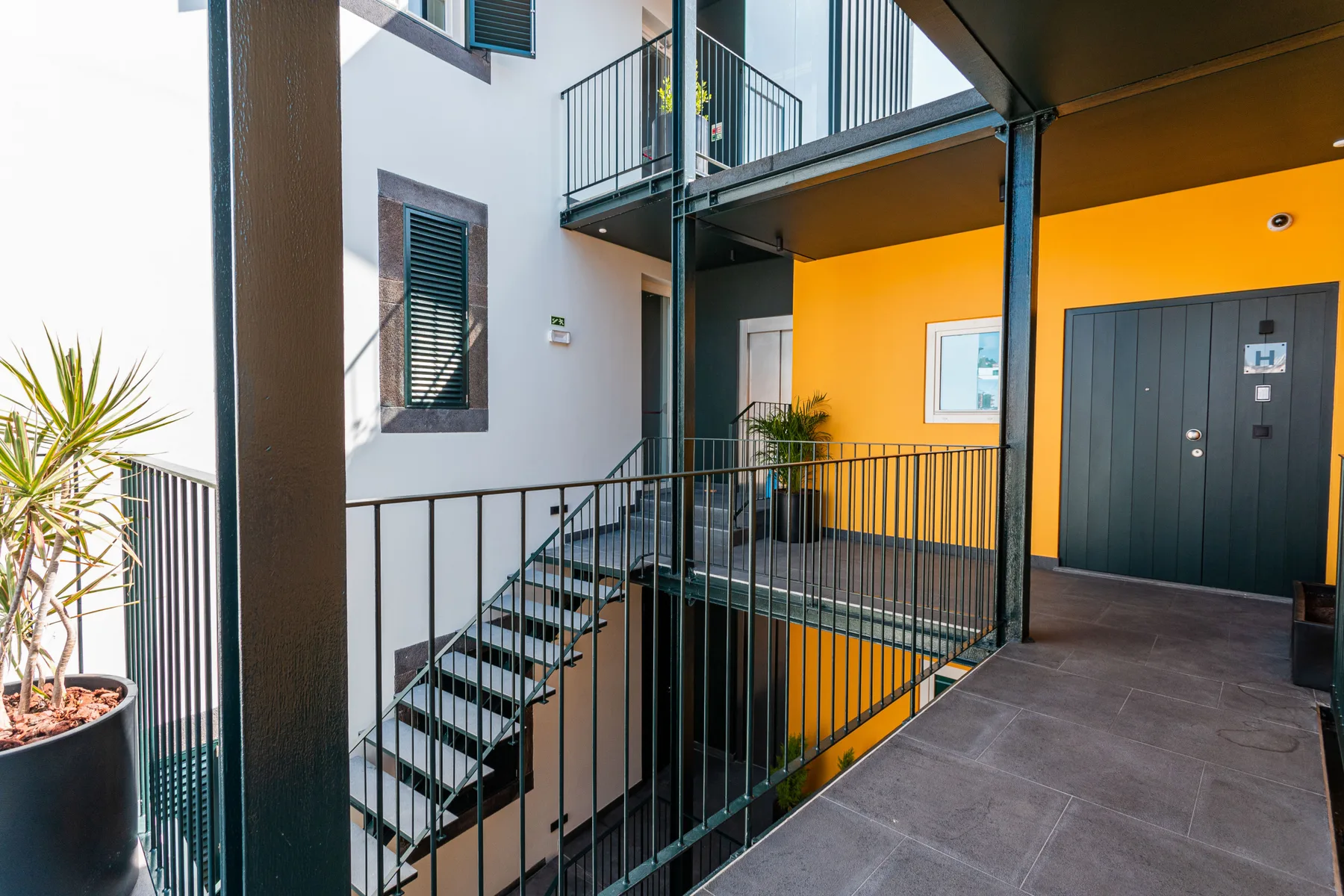 Un pasillo exterior con barandillas metálicas y escaleras junto a una pared naranja.
